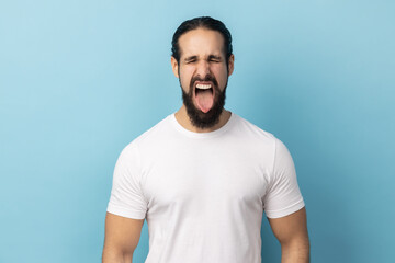 Portrait of playful cheerful man with beard wearing white T-shirt showing tongue, having fun,...