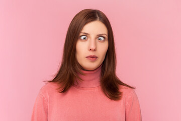 Attractive funny silly woman with brown hair with cross eyed, has stupid dumb face, awkward confused comical expression, wearing rose turtleneck. Indoor studio shot isolated on pink background - obrazy, fototapety, plakaty