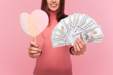 Unknown smiling woman with brown hair holding little pink heart on stick and fan of dollar...