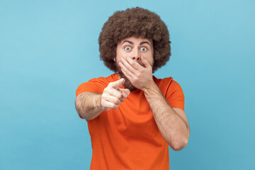 Portrait of shocked man with Afro hairstyle wearing orange T-shirt looking with big eyes and open...