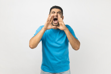 Portrait of unshaven man wearing blue T- shirt standing screams loudly, expresses irritation, keeps...