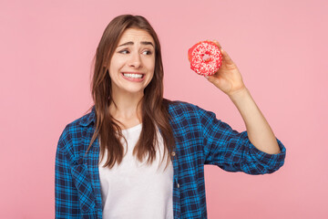Portrait of funny brown haired woman holding donut looking away thinking eat or not keeps diet...