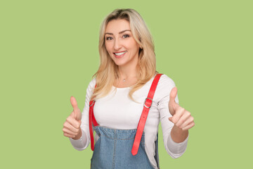 Portrait of smiling delighted adult blond woman showing thumbs up, like gesture, positive feedback,...