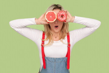 Portrait of shocked surprised adult blond woman standing covering eyes with grapefruit and...