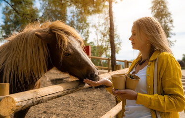 A woman feeds a horse on a farm.