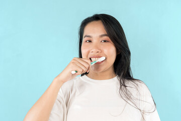 A woman is brushing her teeth with a green toothbrush. She has a smile on her face.