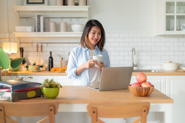 attractive smart asian adult female wear casual cloth working form home using laptop smartphone device,asian female woman work in kitchen island home studio office online hand use smartphone at home © whyframeshot