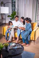 Indian asian young family reading book or looking at photo in album at home