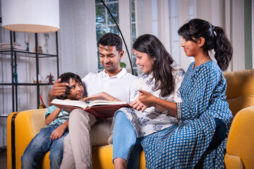 Indian asian young family reading book or looking at photo in album at home