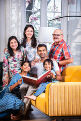 Indian asian kids with parents and grand parents sitting on sofa and watching photos in album or reads book