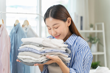 Smile happy asian housewife smelling the scent of fresh clean clothes after laundry