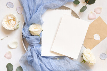Cards near blue tulle fabric knot and cream roses on plates top view copy space, wedding mockup