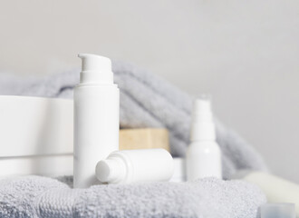 White one pump cosmetic bottles on grey folded towel near basin in bathroom, mockup