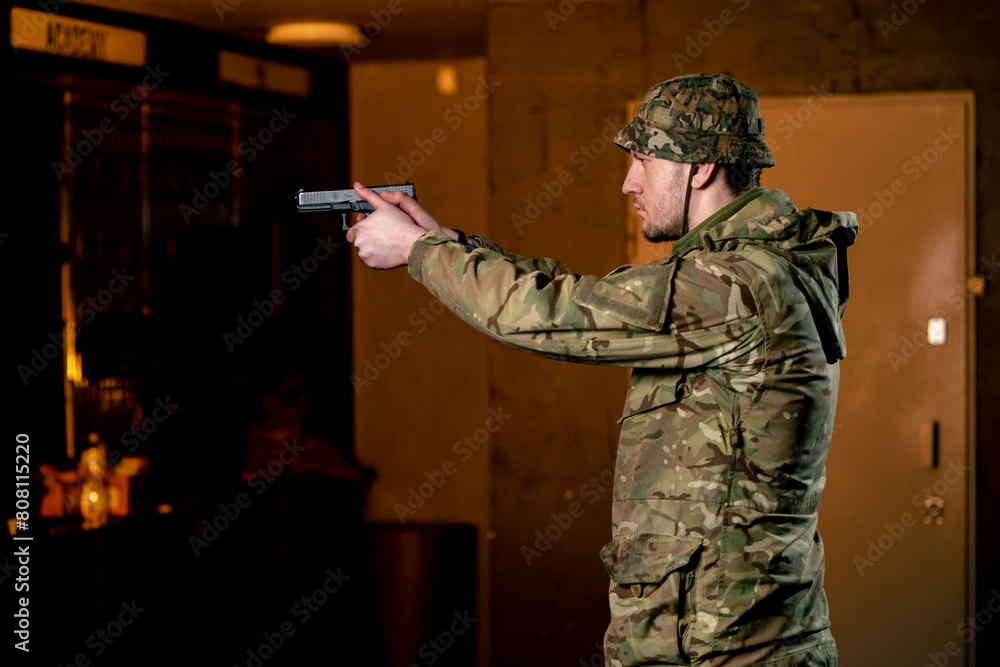 Wall mural In a professional shooting range a military man in ammunition takes aim from a cleaned pistol