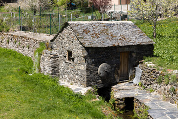 Traditional small stone water mill on a bright sunny spring day next to stream with green vegetation in Tormaleo village Asturias