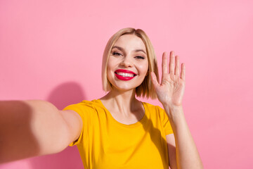 Photo of sweet friendly lady dressed yellow t-shirt recording video waving arm hi isolated pink...