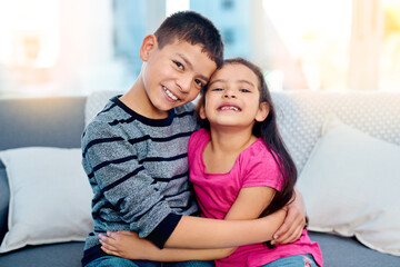 Siblings, hug and portrait of kids in home on sofa to relax with care or support of happy family. Girl, brother or children embrace with love, kindness or friends on holiday and vacation in Mexico