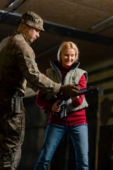 At a professional shooting range military trainer teaches a cheap girl how to hold a NATO rifle correctly