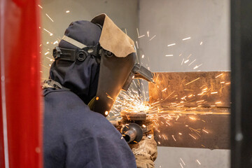 A skilled welder in protective gear works attentively with metal, creating intense sparks while...