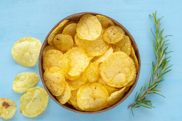 Homemade potato chips in coconut bowl over blue wooden background.