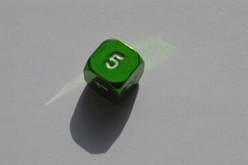 Green D6 die showing 5 in sunlight on white background