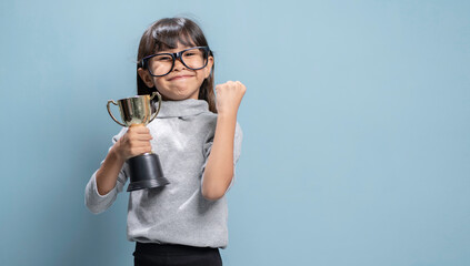 A little girl is holding a gold trophy and is very happy.