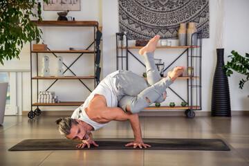 Fit man performing Crow pose on yoga mat at home