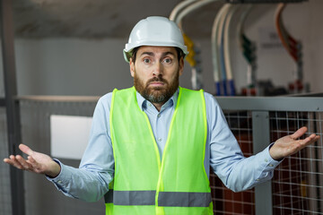 Young handsome worker man wearing green safety vest uniform and helmet clueless and confused...