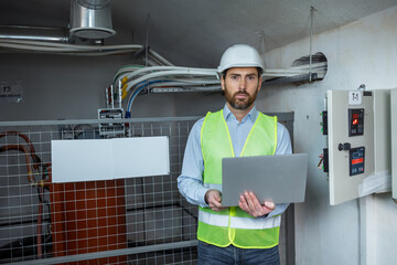 Confident engineer holding laptop computer in a electric supply room.
