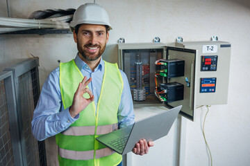 Professional inspector electrician technician engineer in safety uniform holding laptop showing ok sign