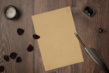 Vintage quill pen and empty old blank paper sheet with rose petals on wooden background from above....