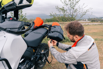 Motorcyclist packing bags on Adventure motorcycle in moto tour in beautiful mountains