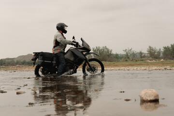 Motorcyclist traveling on adventure motorcycle crossing river in mountains
