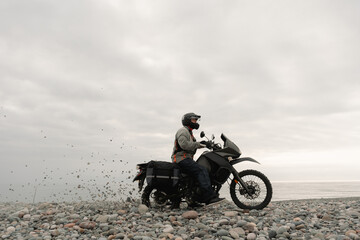 Motorcyclist traveling on adventure motorcycle towing on  seashore pebbles