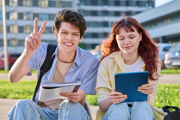 Teenage college students guy and girl talking, sitting outdoor