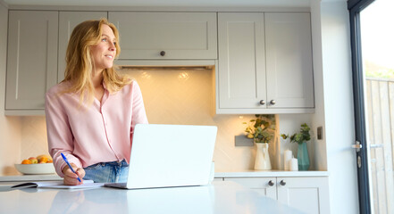 Smiling Woman Working From Home In Kitchen Using Laptop