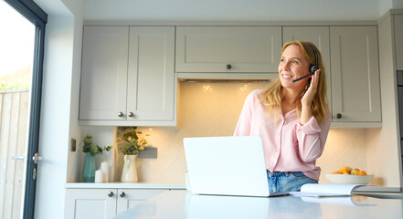 Woman Wearing Headset Working From Home In Kitchen Using Laptop - Powered by Adobe