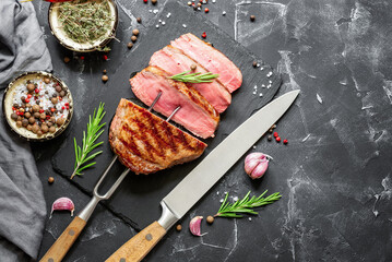 Beef steak medium rare on the grill, black stone background. Top view, flat lay, copy space. Steak on a meat fork and a knife