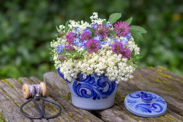 Blumen-Arrangement mit Holunderblüten, Klee und Vergissmeinnicht im rustikalen Töpfchen