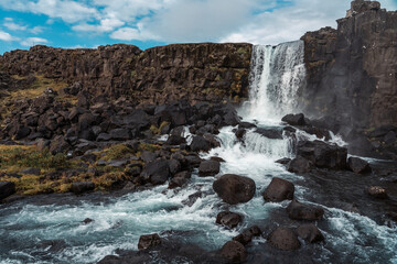 Oxararfoss, spectacular Icelandic waterfall. Þingvellir National Park. Cold water falls on large black boulders of volcanic origin.