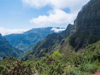 View of green hills, mountain landscape in clouds at blue sky. and lush vegetation at hiking trail PR12 to Pico Grande one of the highest peaks in the Madeira, Portugal