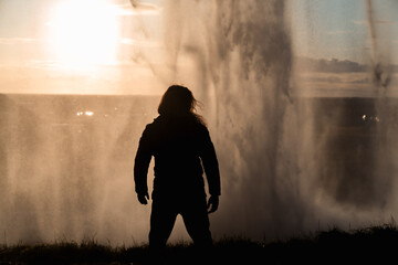 Person in silhouette under a huge waterfall. Hiker posing at sunset behind the Seljalandsfoss...