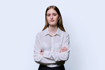 Portrait of teenage serious female in white shirt with crossed arms on studio background