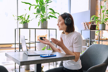 Young woman in headphones having video chat conference using laptop sitting in cafe