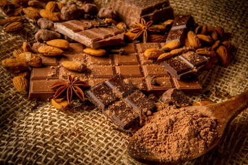 Still life of chocolate bar with cocoa powder in a dipper with almonds and spices