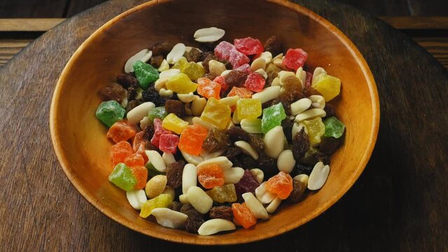 Mix of multi-colored dried fruits, candied fruits and scattered nuts in a wooden plate, rotating in a circle. Medium plan