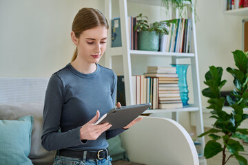 Young female teenager with digital tablet, stylus drawing illustrating sitting at home