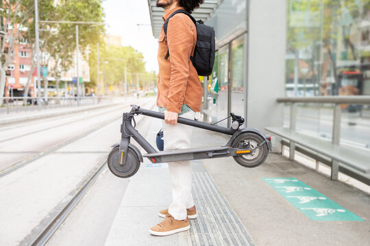 Man holding a folded electric scooter on a city sidewalk