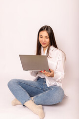 Naklejka premium A young woman in white shirt with a laptop sits on white background.Work online