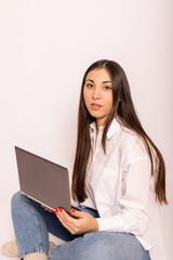 A young woman in white shirt with a laptop sits on white background.Work online